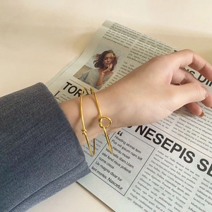 Detail view of two gold knotted cuff bracelets on a vintage newspaper background