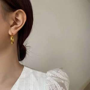 Close-up of a polished gold hoop earring worn by a model to show the size and shiny texture