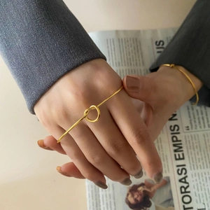 Detail of a gold knotted cuff bracelet worn with a smart blazer for a chic, minimalist look