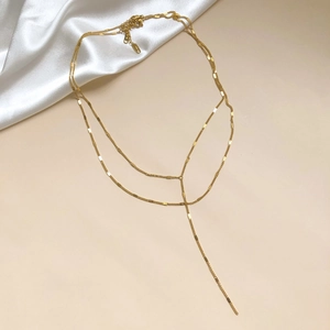 Vue macro d'un collier lariat doré à plusieurs rangs avec chaîne plate et détail de pompon