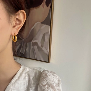 Close-up of polished gold hoop earring worn by a model in a minimalist artistic setting
