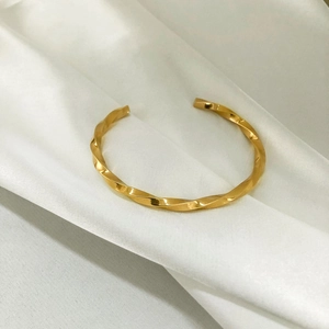 Nahaufnahme eines goldenen Möbius-Armreifs mit Spiraltextur auf weißem Seidenstoff