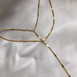 Détail d'un collier en Y doré superposé sur un fond en tissu satiné blanc