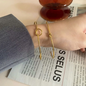 Close-up of gold knot and interlocking open cuff bracelets worn with a grey suit