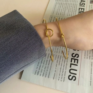 Detailed view of two gold knotted bracelets paired with a grey suit sleeve for a chic look