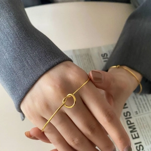 Close-up of a minimalist gold knot cuff bracelet worn on a wrist with an elegant suit