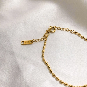 Macro shot of 18K gold bracelet featuring oval beads and K18 hallmark on silk