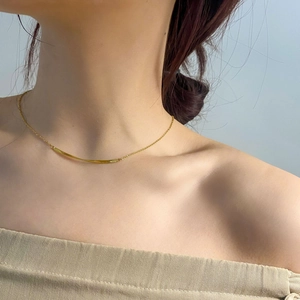 Detailansicht einer minimalistischen goldenen Halskette mit geschwungenem Stabanhänger