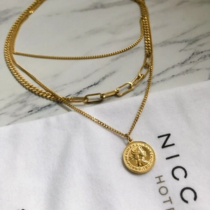 Dettaglio della collana a tre strati dorata con ciondolo a moneta e maglie spesse