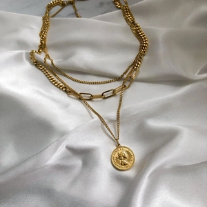 Dettaglio della collana dorata a più strati con pendente a moneta su seta bianca