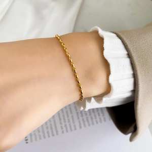Detail shot of delicate gold beaded bracelet with oval-shaped links on a model's wrist