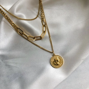 Collana a strati dorata con ciondolo a moneta e catene a maglie su sfondo di seta