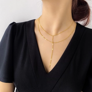 Détail d'un collier doré double épaisseur à pampilles Y sur un haut noir élégant