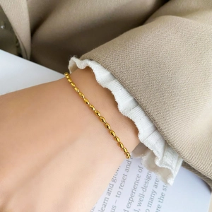 Close-up of a minimalist gold rice bead bracelet worn on a wrist over a magazine