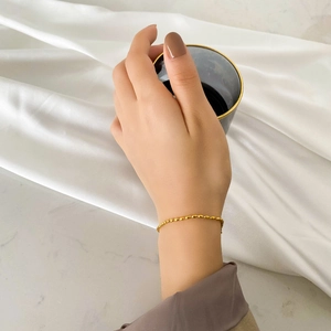 Detailed shot of a minimalist gold beaded bracelet worn on wrist with elegant silk backdrop