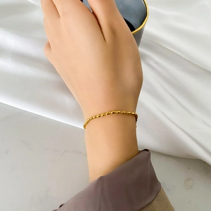 Minimalist gold oval bead chain bracelet worn on wrist over elegant silk fabric