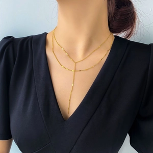 Détail d'un collier en Y doré à deux rangs porté sur un vêtement noir élégant