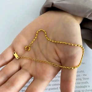 Macro shot of gold oval bead chain bracelet with adjustable spring clasp and tag detail