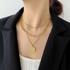 Dettaglio di collane dorate a strati con maglie spesse e ciondolo a moneta vintage