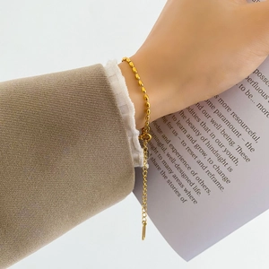 Detail of minimalist gold beaded bracelet on wrist with elegant suit sleeve and paper props