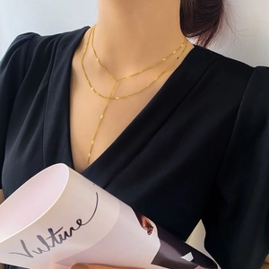 Gros plan sur un collier en Y doré minimaliste porté sur un haut noir à col en V élégant