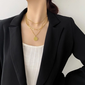 Dettaglio collana dorata a più strati con catena a maglie ovali e ciondolo a moneta