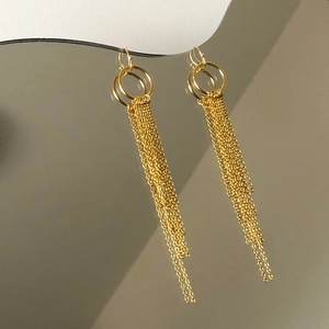 Gros plan détaillé de longues boucles d'oreilles à pompons dorés avec anneaux entrelacés