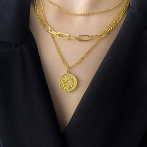 Dettaglio di collane d'oro a strati con maglie spesse e ciondolo a moneta sul modello
