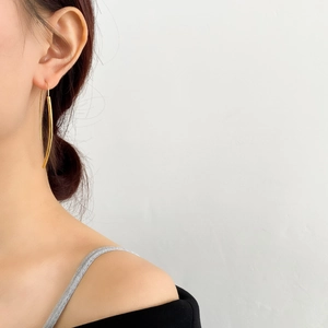 Dettaglio di lunghi orecchini a cerchio dorati ricurvi indossati su modella lucida