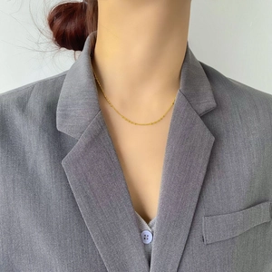 Détail d'un collier à perles dorées fines porté avec un blazer gris pour un look chic