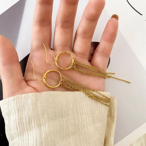 Détail de longues boucles d'oreilles pompons dorées avec crochet élégant à la main