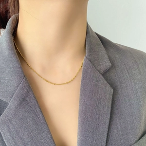 Collier minimaliste plaqué or à perles géométriques porté sur un blazer gris élégant