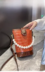 Detail of orange faux crocodile bucket bag featuring pearl handle and golden clover charm
