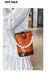 Detail of orange embossed bucket bag featuring pearl handle and gold clover clasp