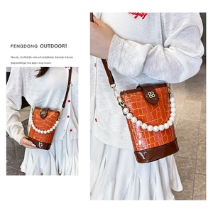 Detail of orange faux-crocodilian bucket bag with pearl handle and metal 88 logo
