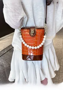 Close-up of orange crocodile texture bucket bag with pearl handle and metal petal buckle