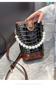 Detail of pearl handle and floral gold clasp on a crocodile pattern bucket bag