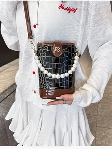 Close-up of black crocodile-patterned bucket bag with pearl chain and gold metal buckle