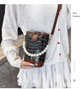 Detail of glossy crocodile pattern bucket bag with pearl handle and golden petal clasp