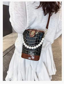 Detail of a black stone-embossed bucket bag with pearl handle and clover metal lock
