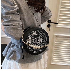 Detail of round black crossbody bag featuring ethnic embroidery and pearl chain