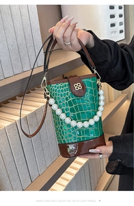 Detail of green faux crocodile bucket bag with pearl handle and golden flower clasp