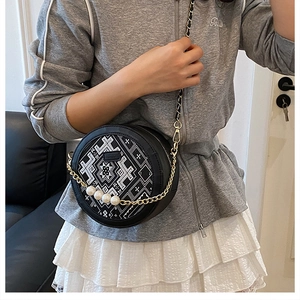 Detail of round crossbody bag with geometric embroidery, gold chain and large pearls