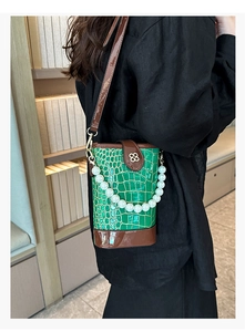 Detail view of green crocodile texture bucket bag with pearl strap and clover hardware