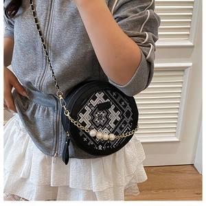 Détail d'un sac rond noir avec broderie géométrique et grandes perles décoratives