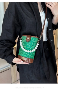 Detail of green crocodile texture bucket bag with pearl handle and golden clover logo