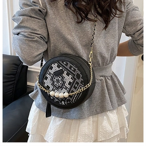 Detail of round crossbody bag with ethnic print, gold chain and luxury pearl strap