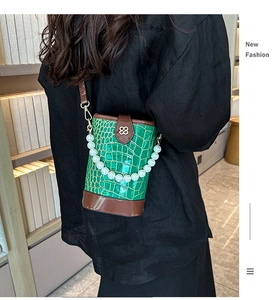 Green crocodile pattern bucket bag with pearl handle worn as a crossbody bag