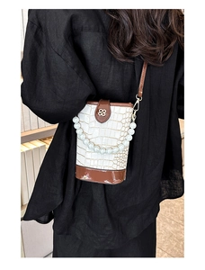 Detail of white crocodile pattern bucket bag with pearl handle and metal buckle on model