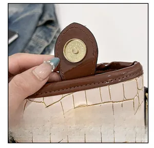 Close-up of golden magnetic buckle on cream faux crocodile leather bucket bag